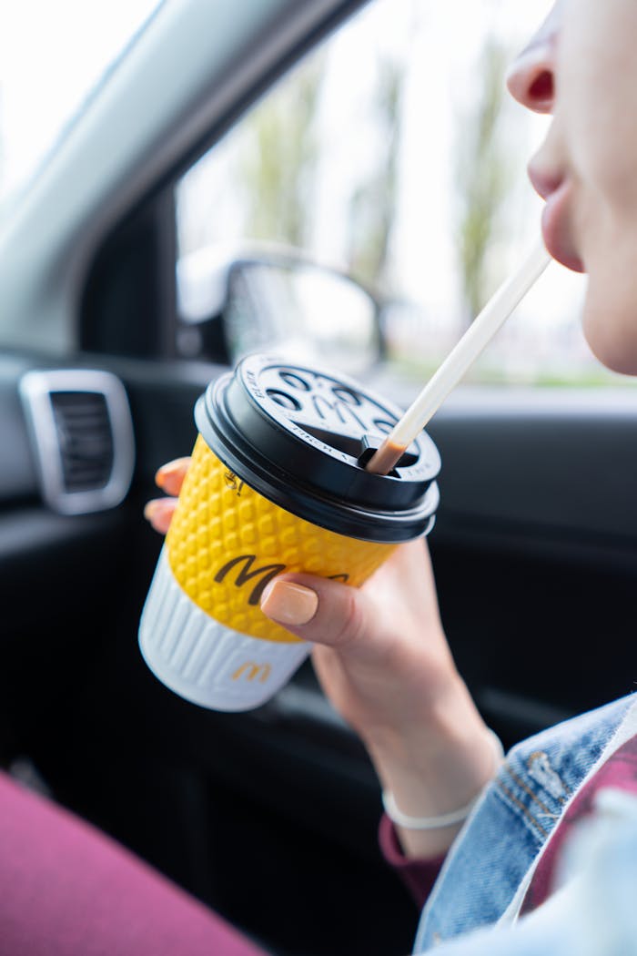 services-02 Close-up of a person sipping coffee from a takeaway cup inside a car on a road trip.