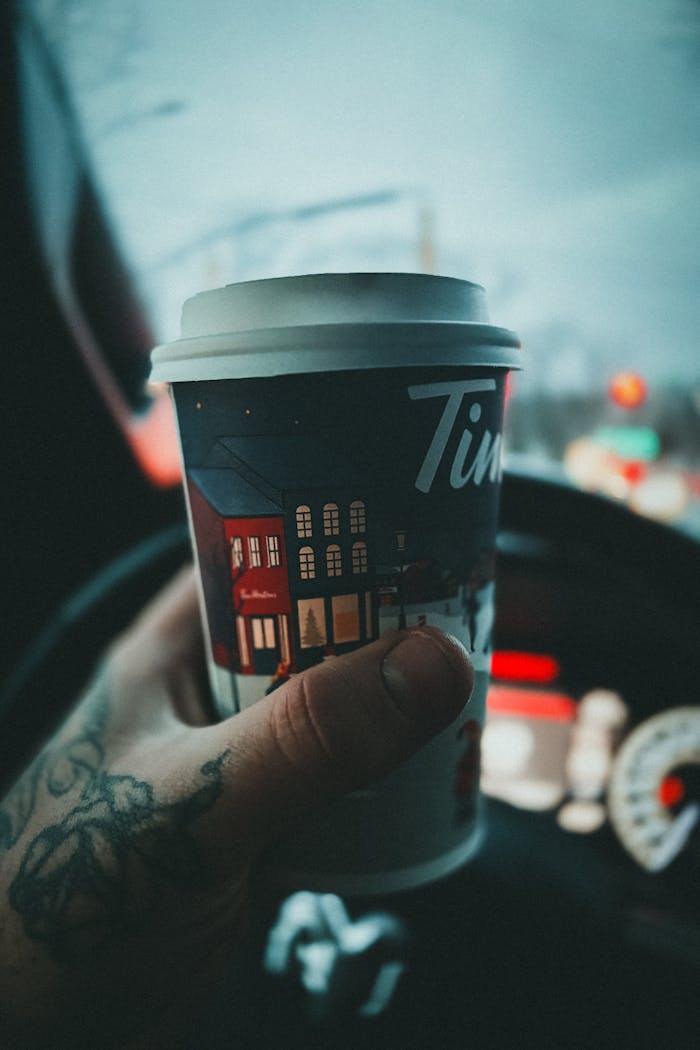 services-03 A tattooed hand holds a festive coffee cup inside a car, showcasing a winter atmosphere.