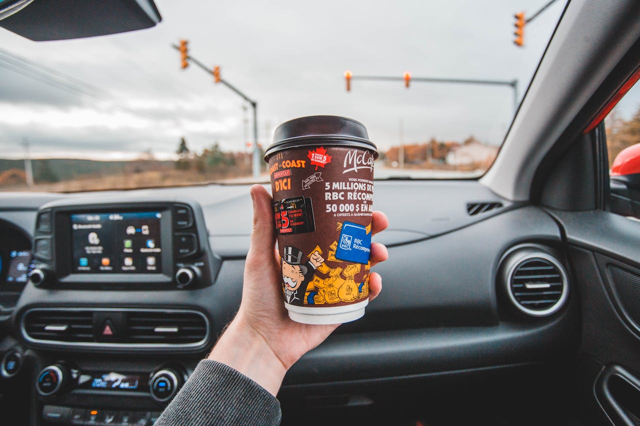 why-choose-us Hand holding coffee cup inside car with intersection view ahead. Captured in overcast weather.