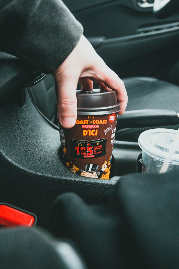 about-02 Close-up of a hand placing a coffee cup in a car holder, emphasizing convenience.
