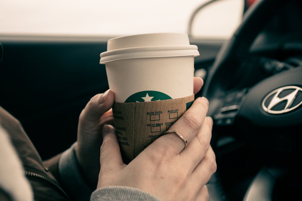 about-01 Close-up of hands holding a coffee cup inside a car, showcasing a modern lifestyle moment.